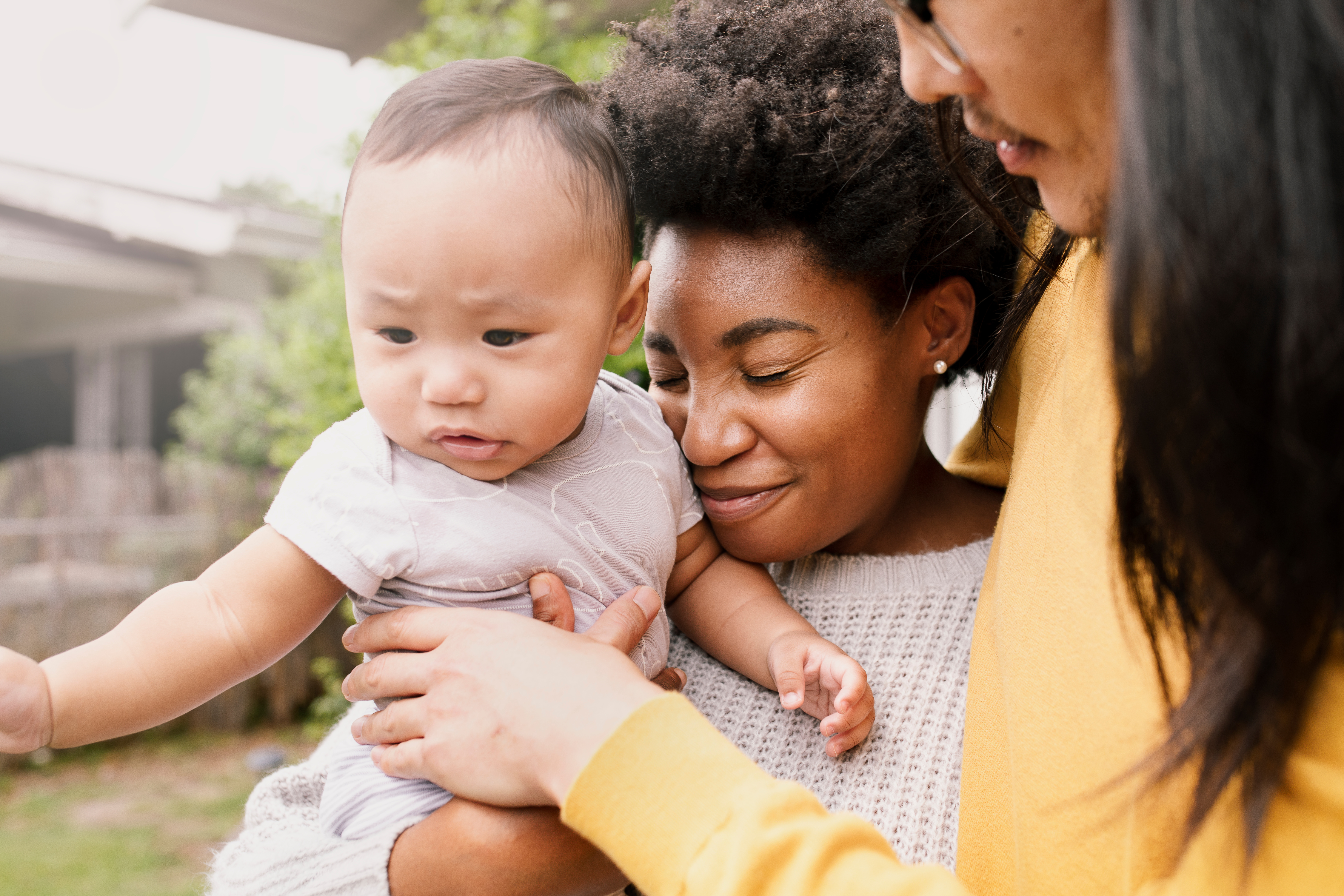 Two people hug a baby close while standing in a backyard