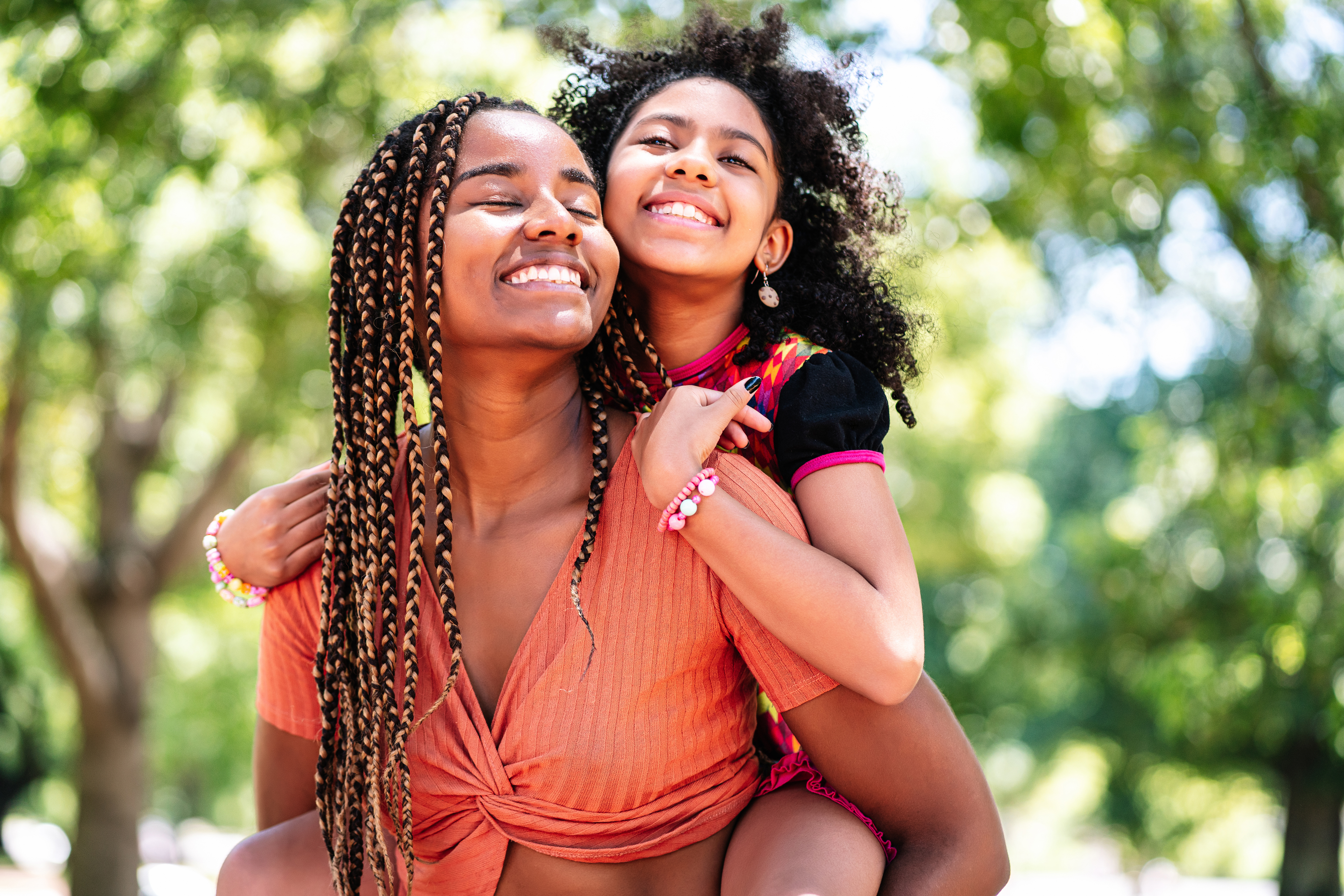 a young woman holds a child on her back and both smile in sunlight