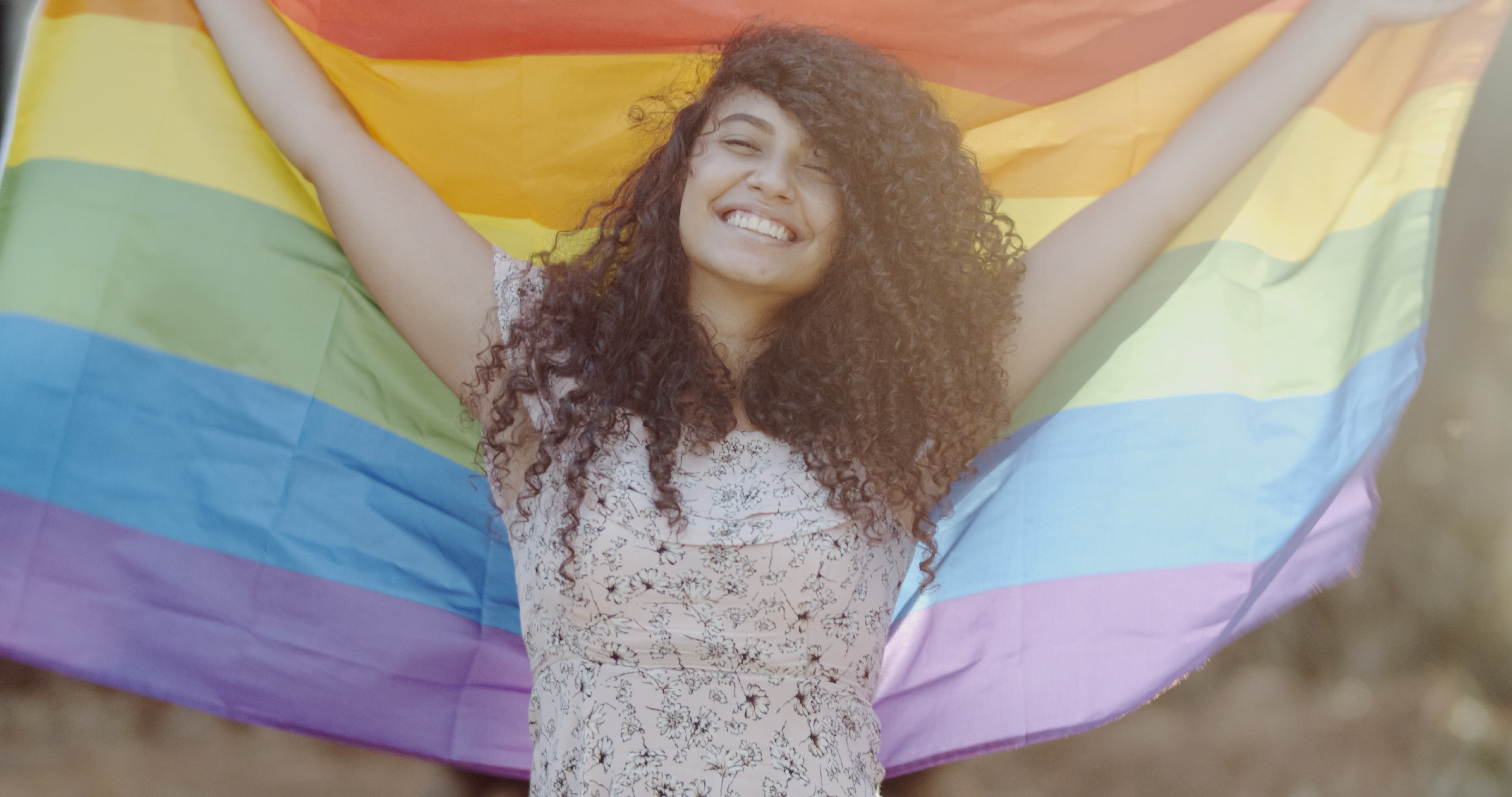 A young person holds up a pride flag and smiles