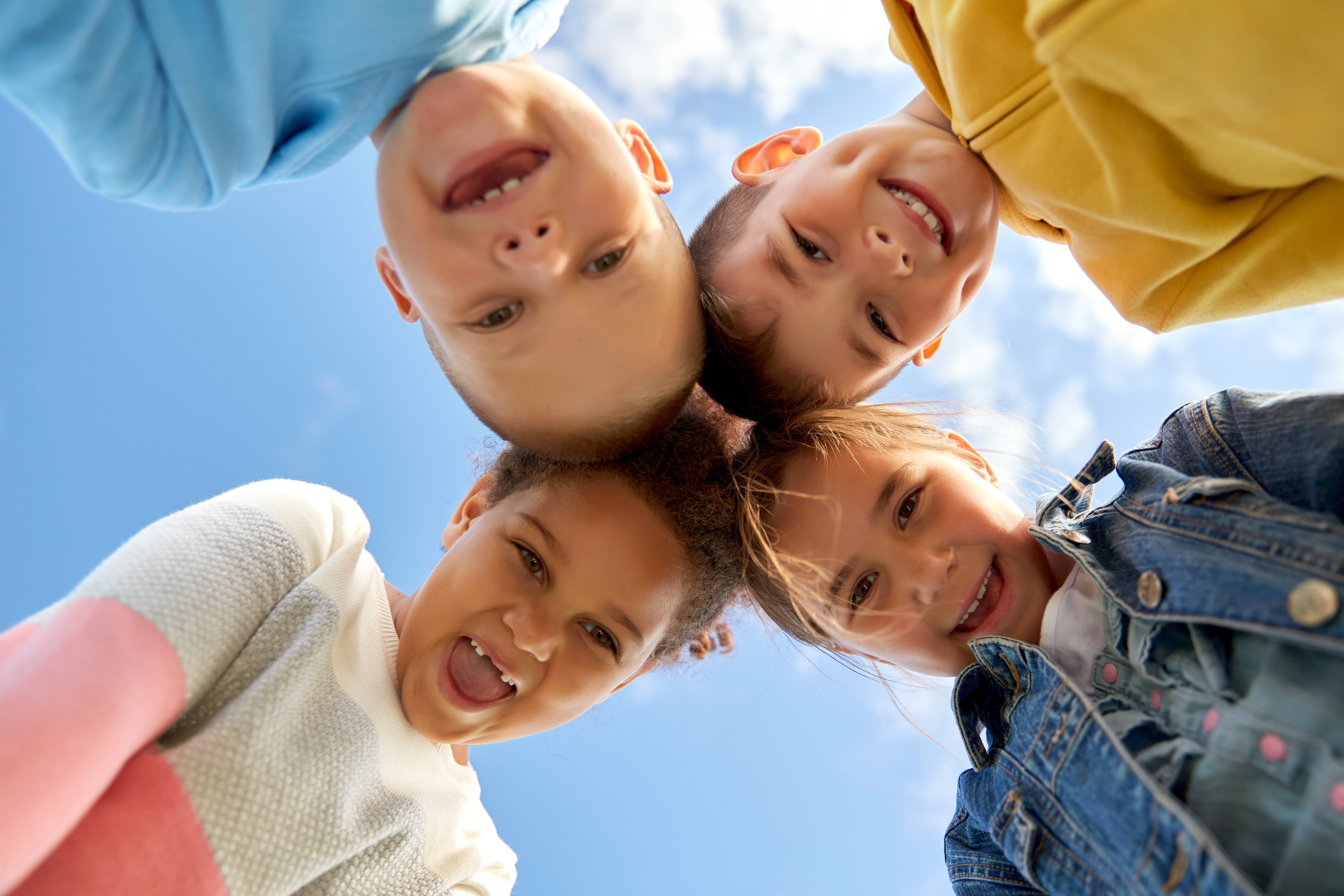 Four kids stare down at the camera against a blue sky