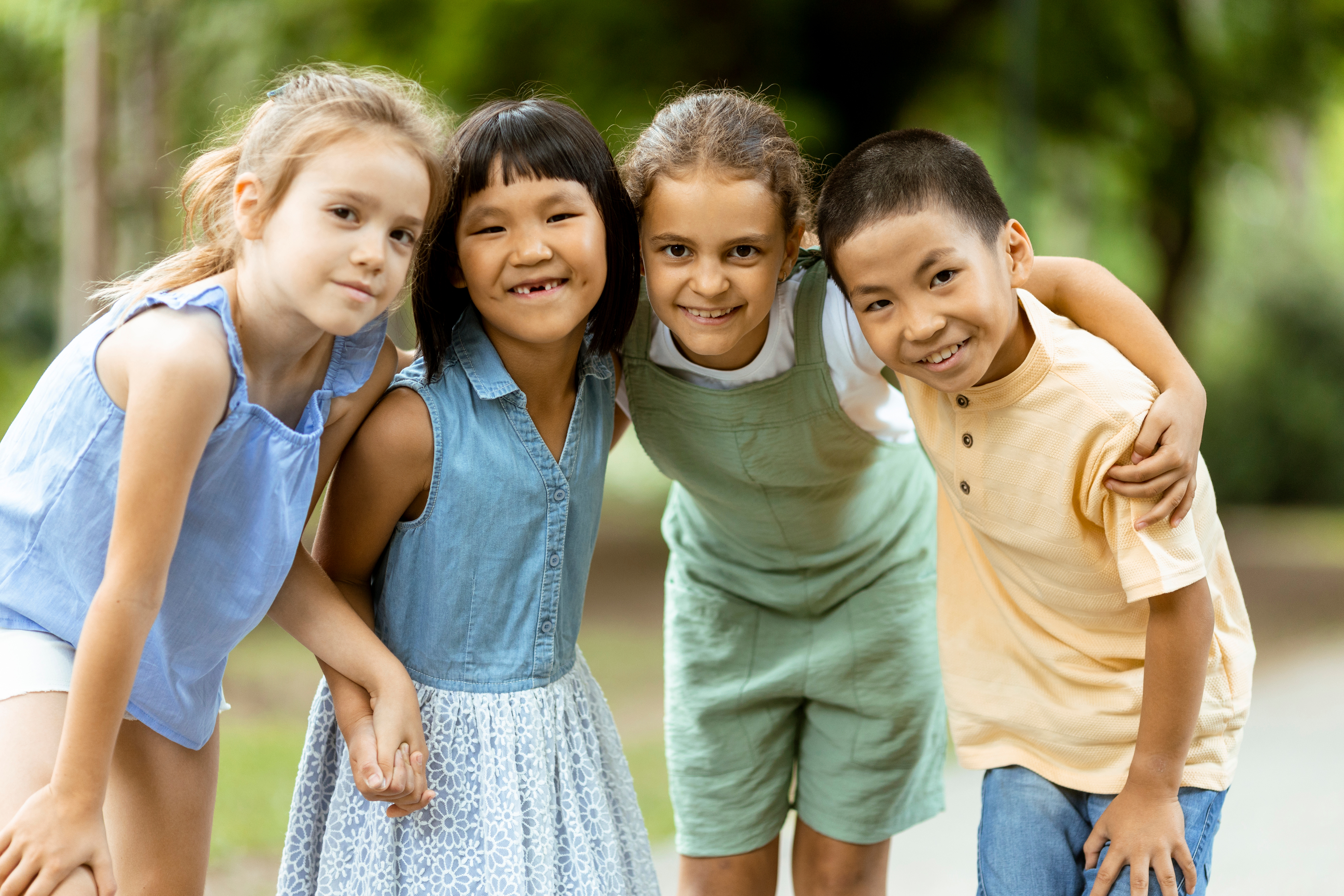 A group of children stand together outside and smile at the camera