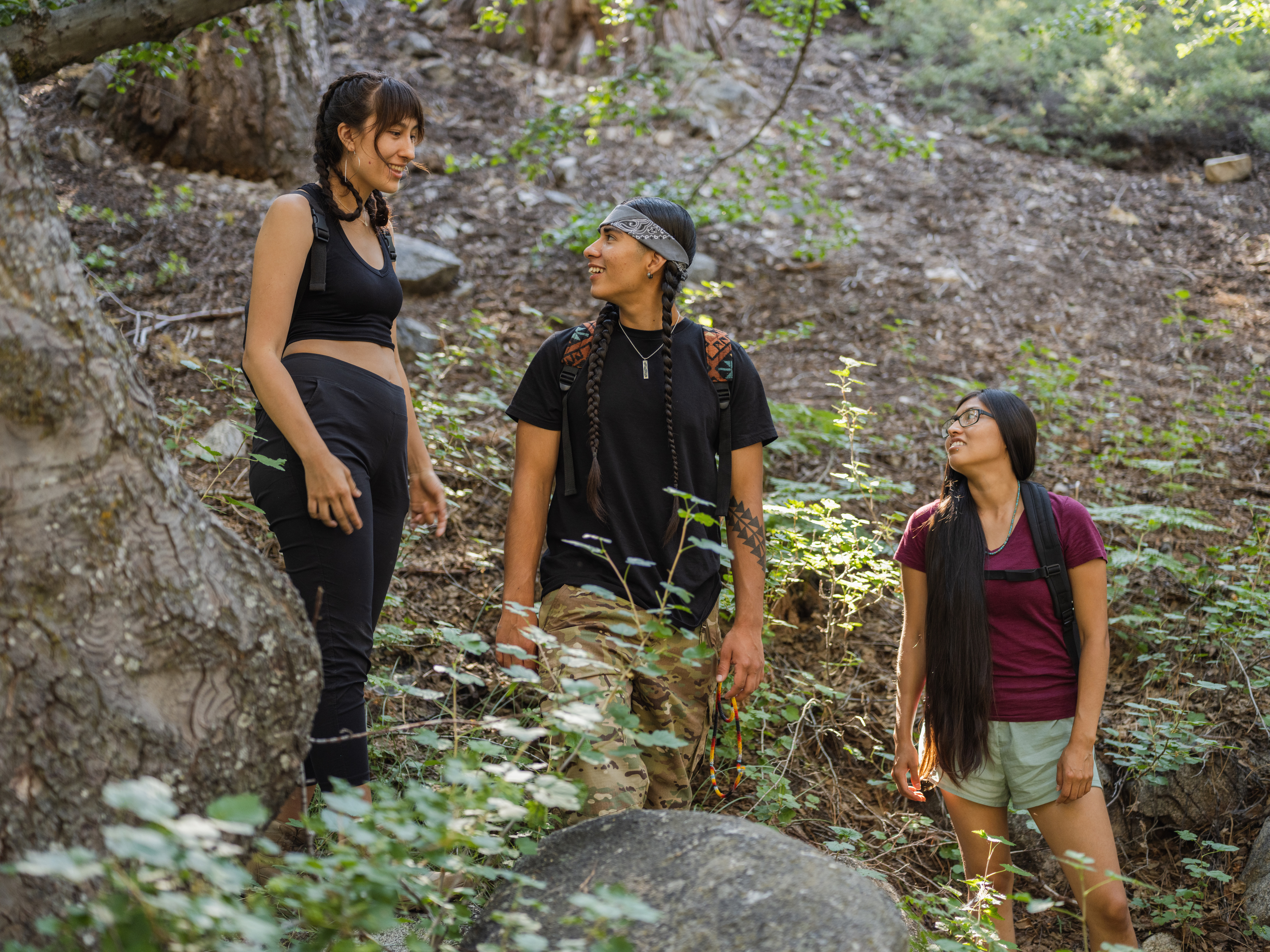 Three teenagers stand in the woods smiling