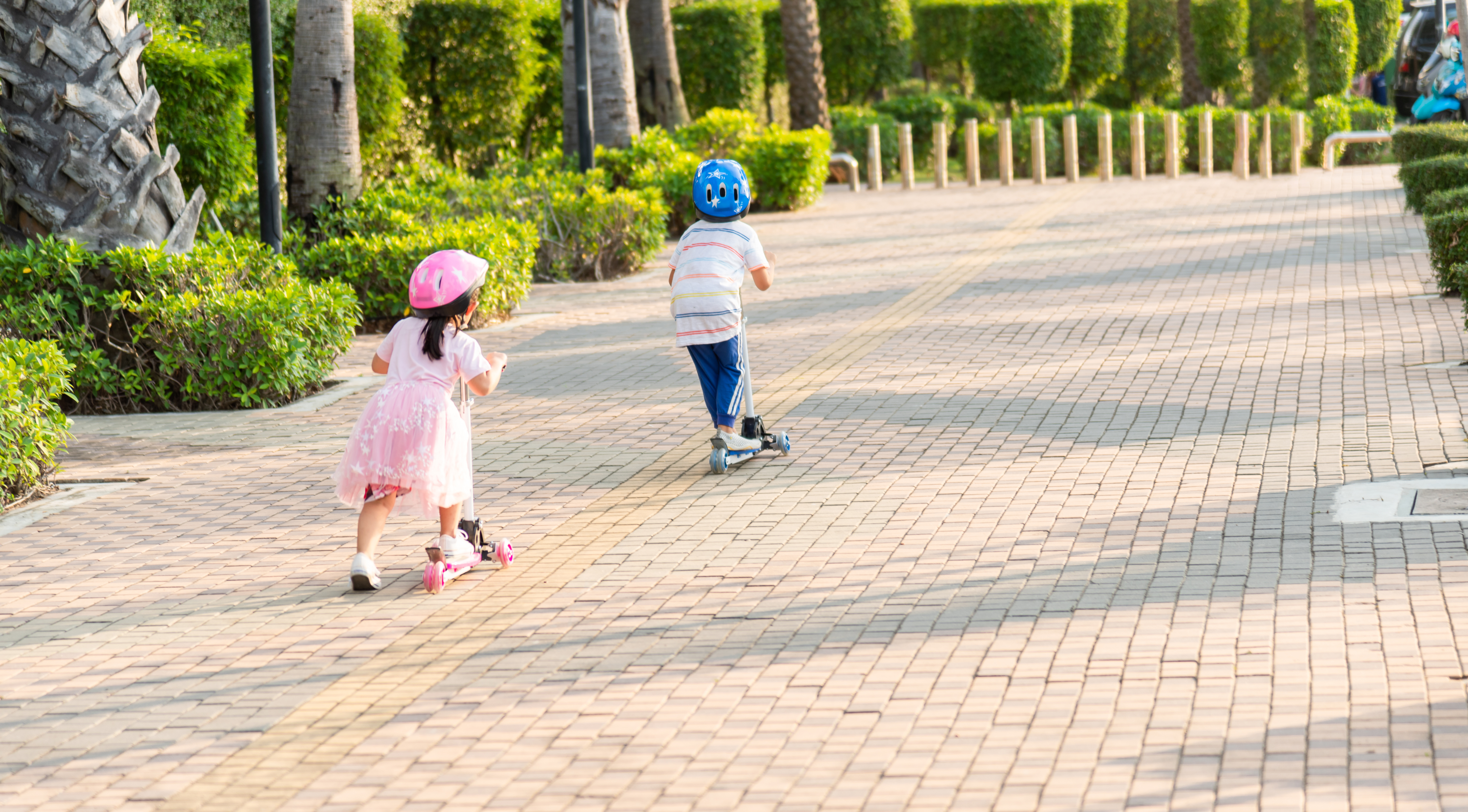 Kids ride scooters down a tree-lined path