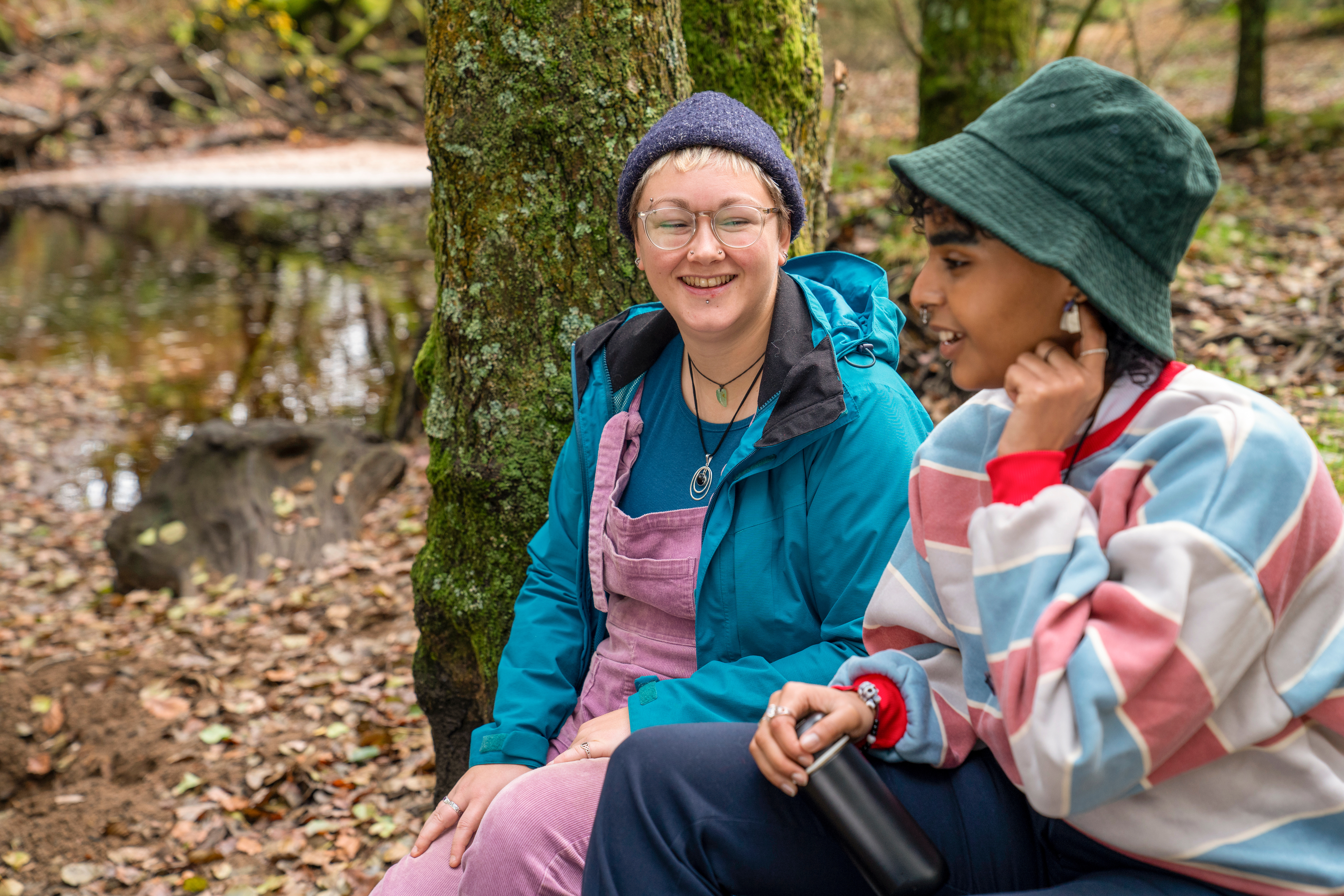 two young people sit side by side in the woods