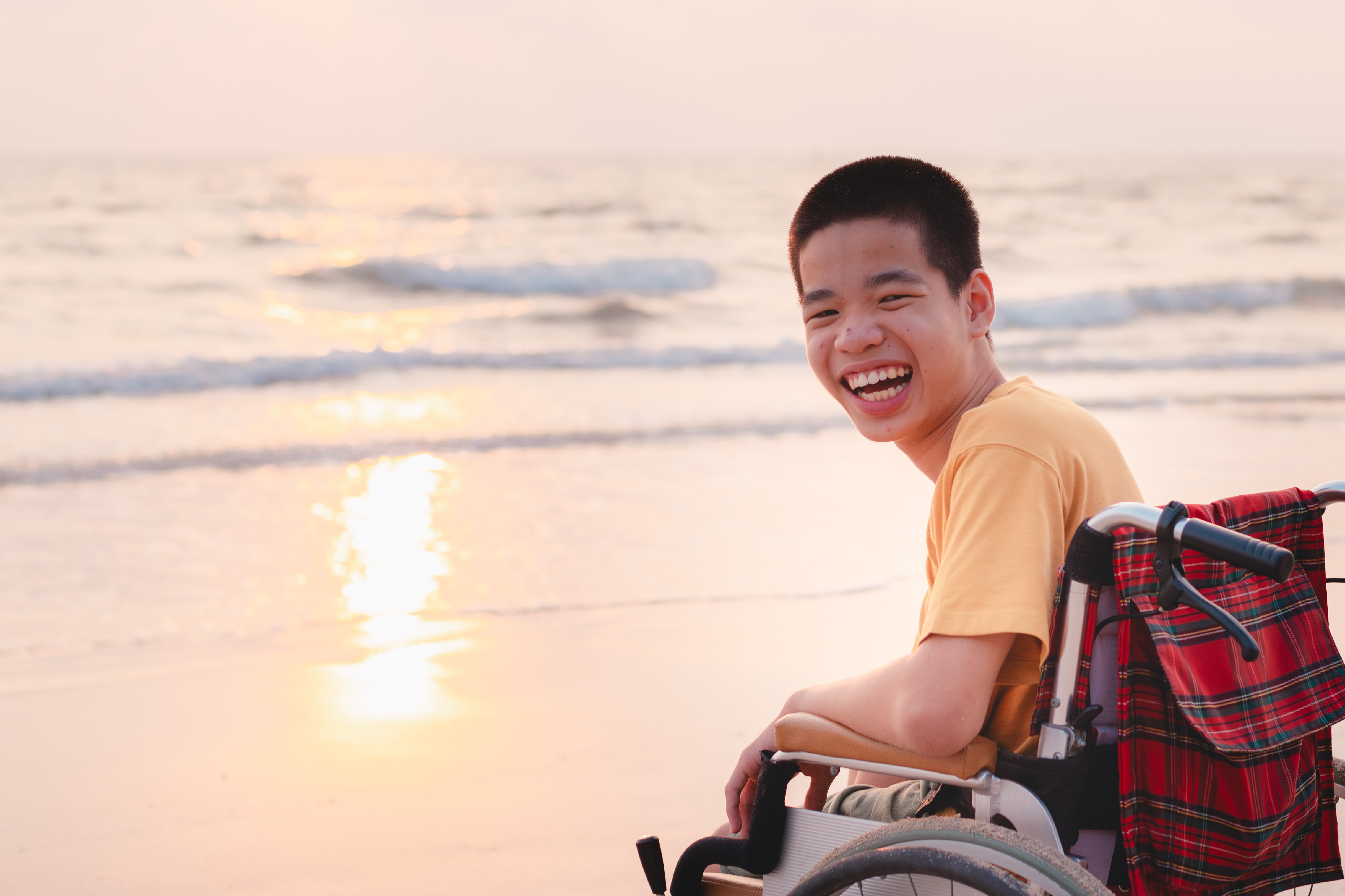 a young man in a wheelchair smiles on the beach