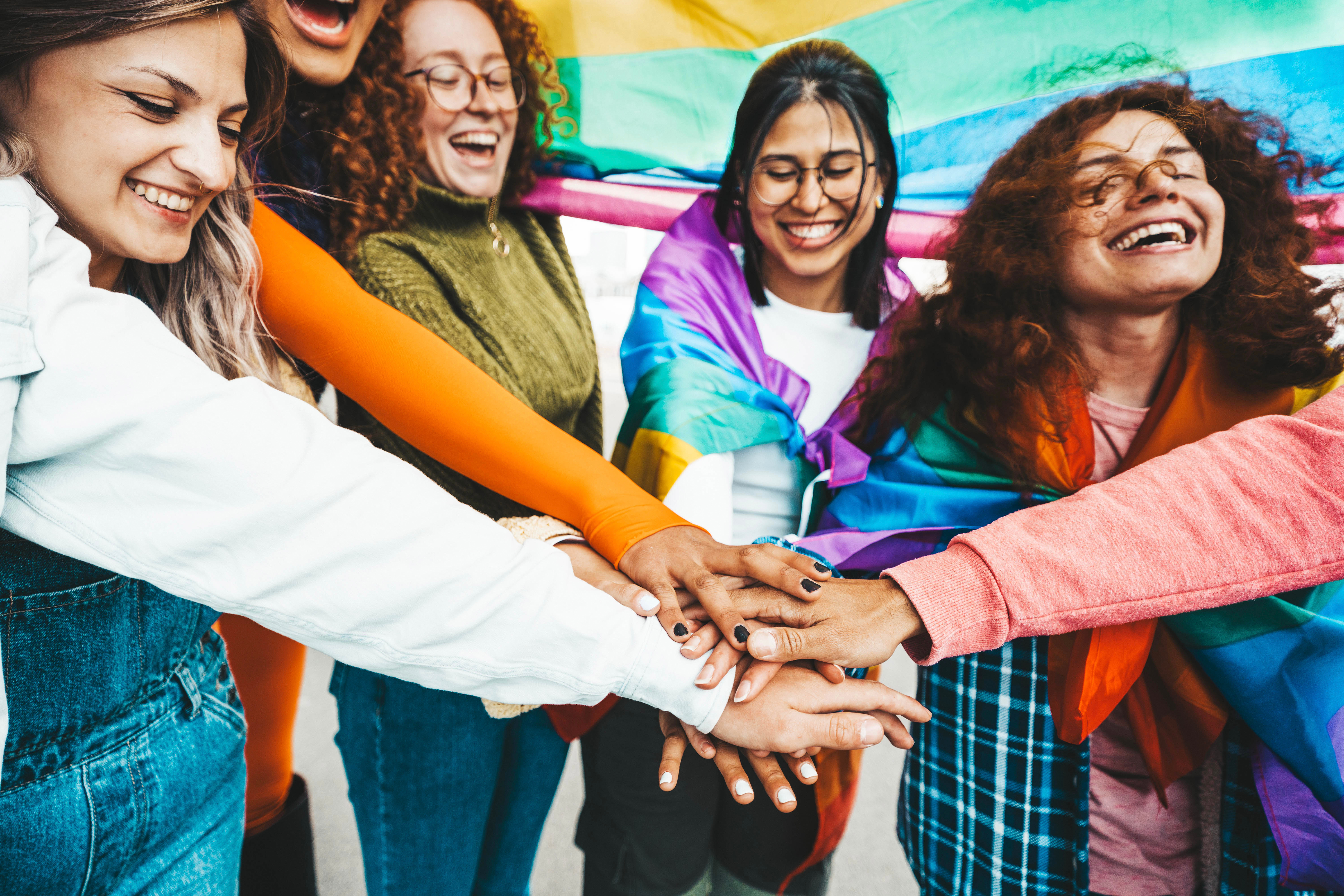 a group of youth put their hands in together while wearing pride flags