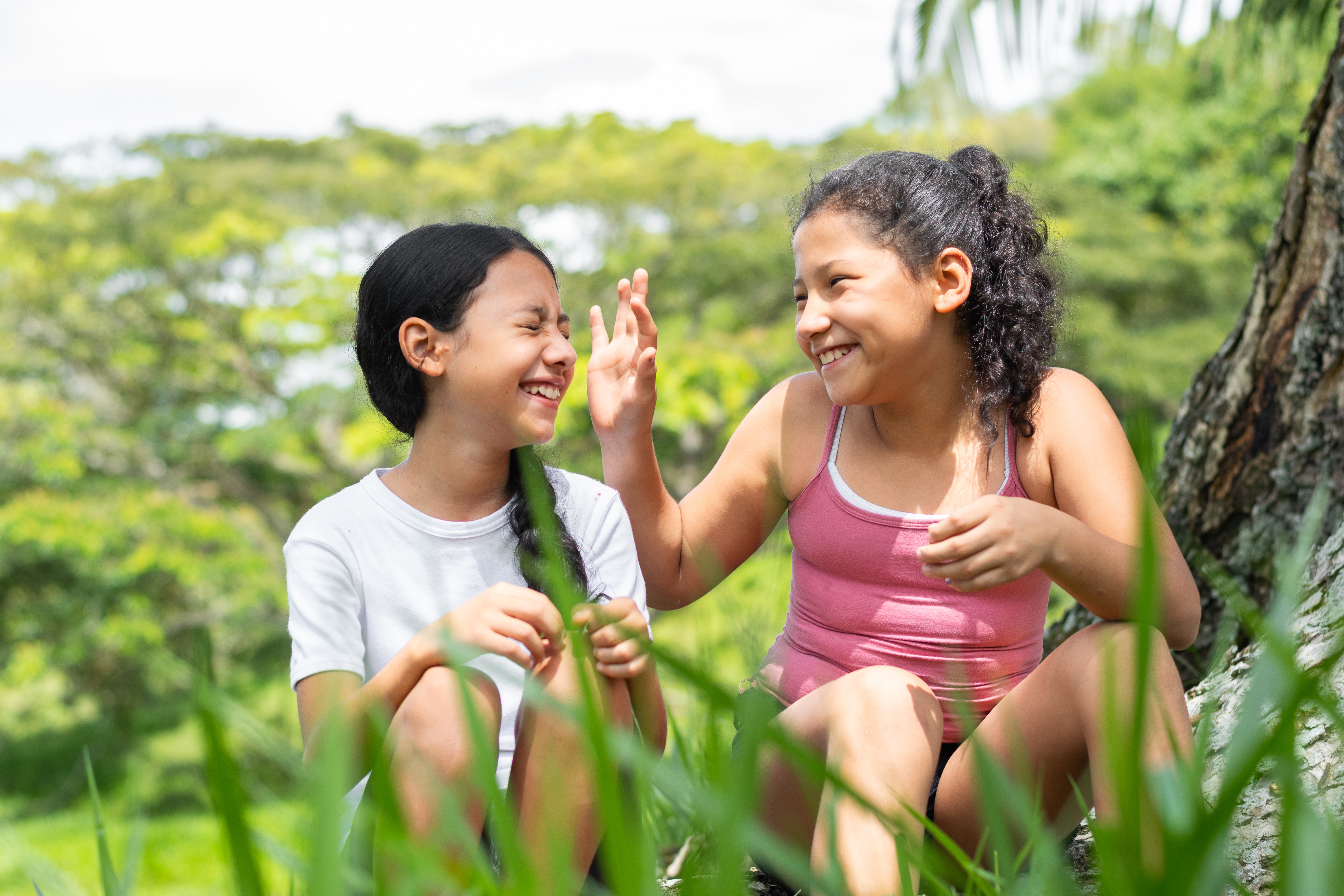 Two kids sit in the grass together and smile