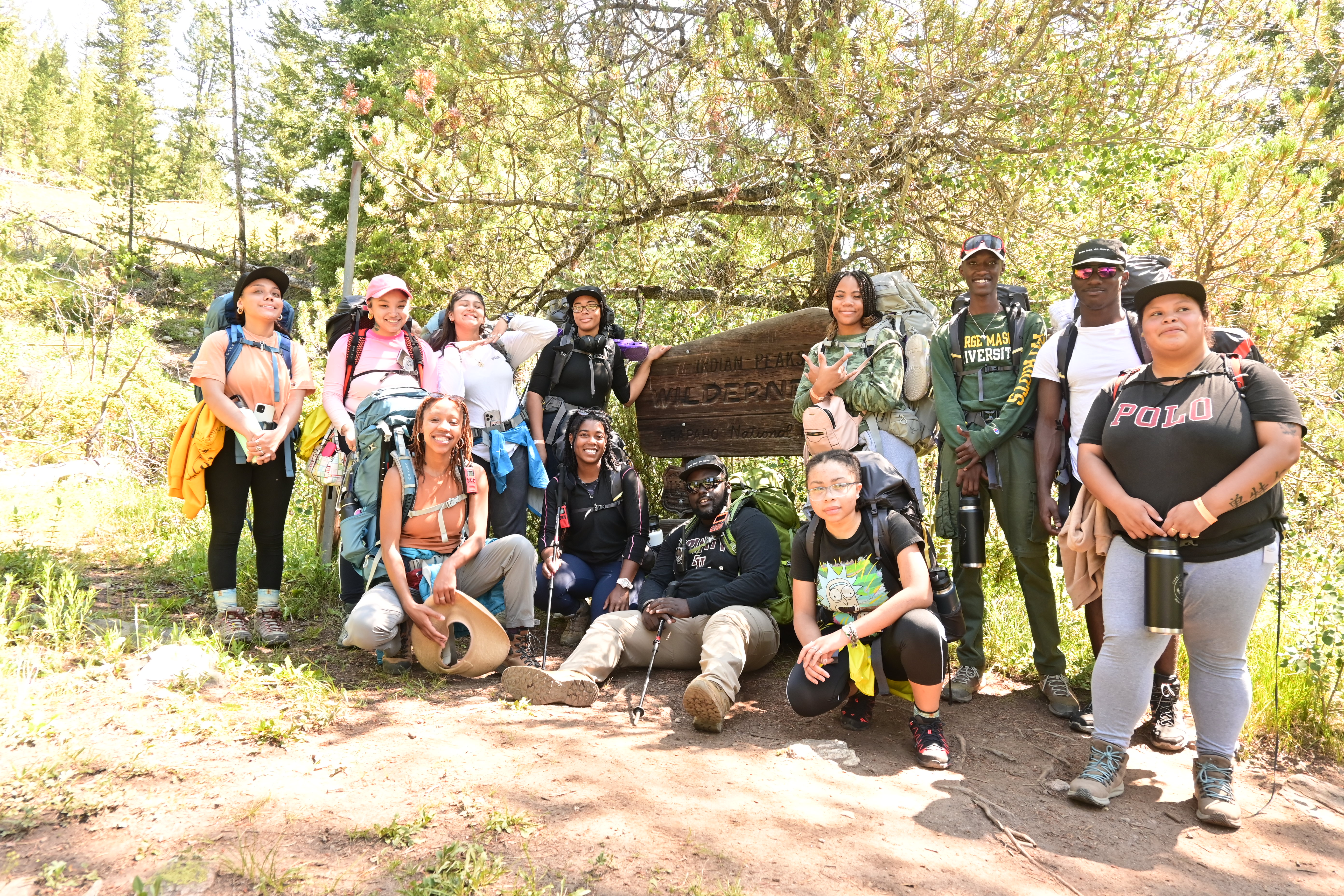A group of youth wearing backpacks stands next to a wilderness sign. 
