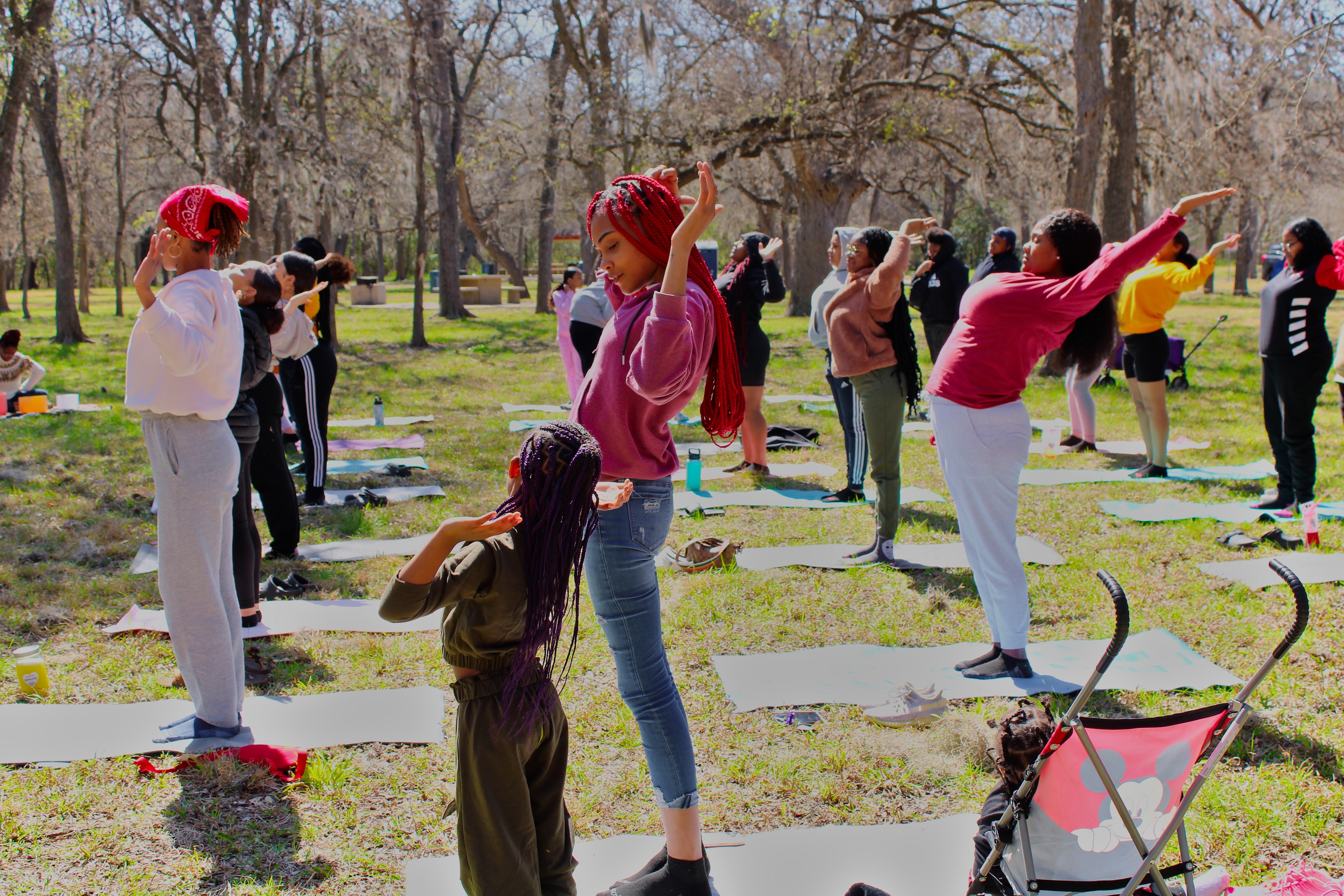 A group of people stretches in a park while standing on yoga mats