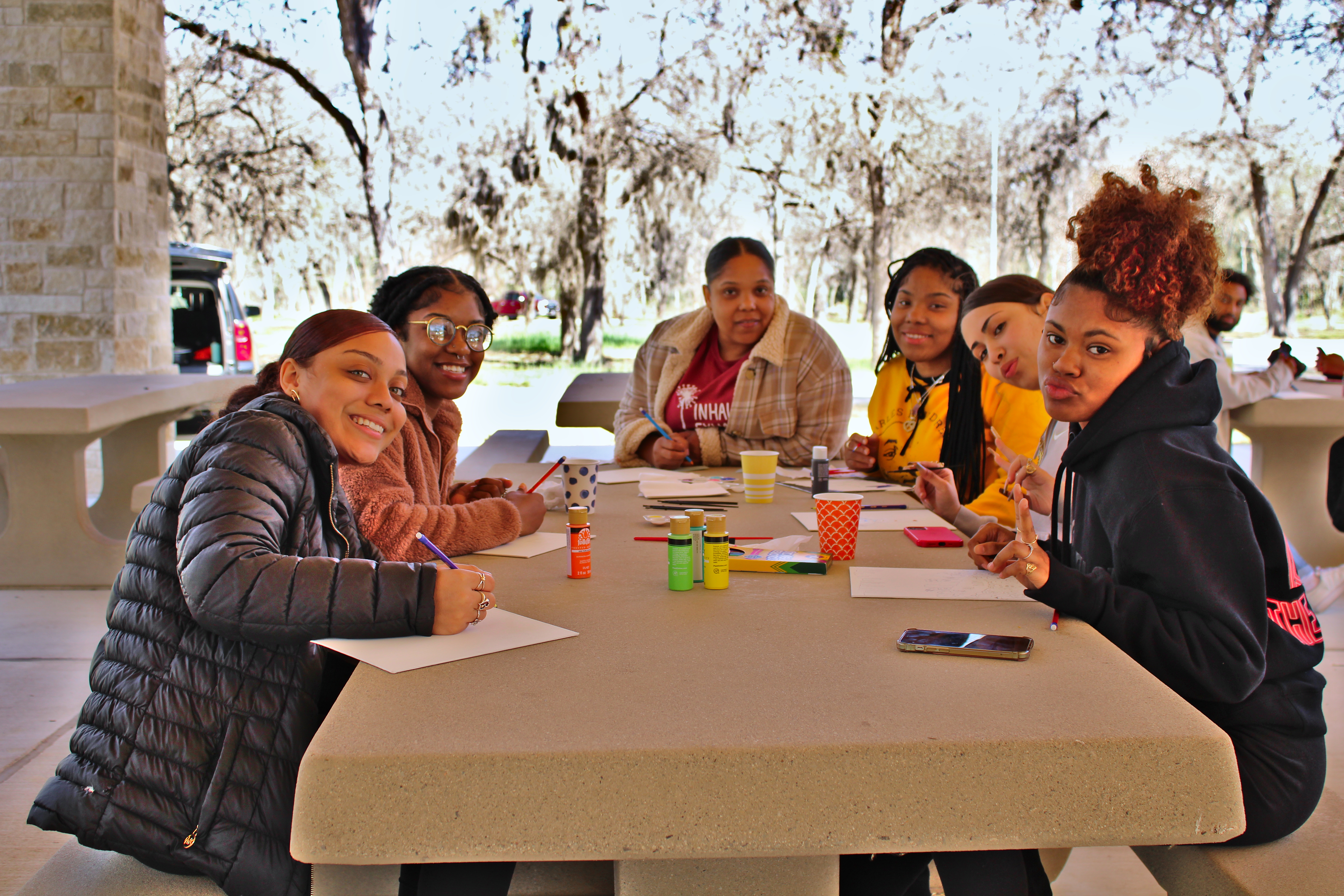 A group of young women sit around a picnic table and smile at the camera