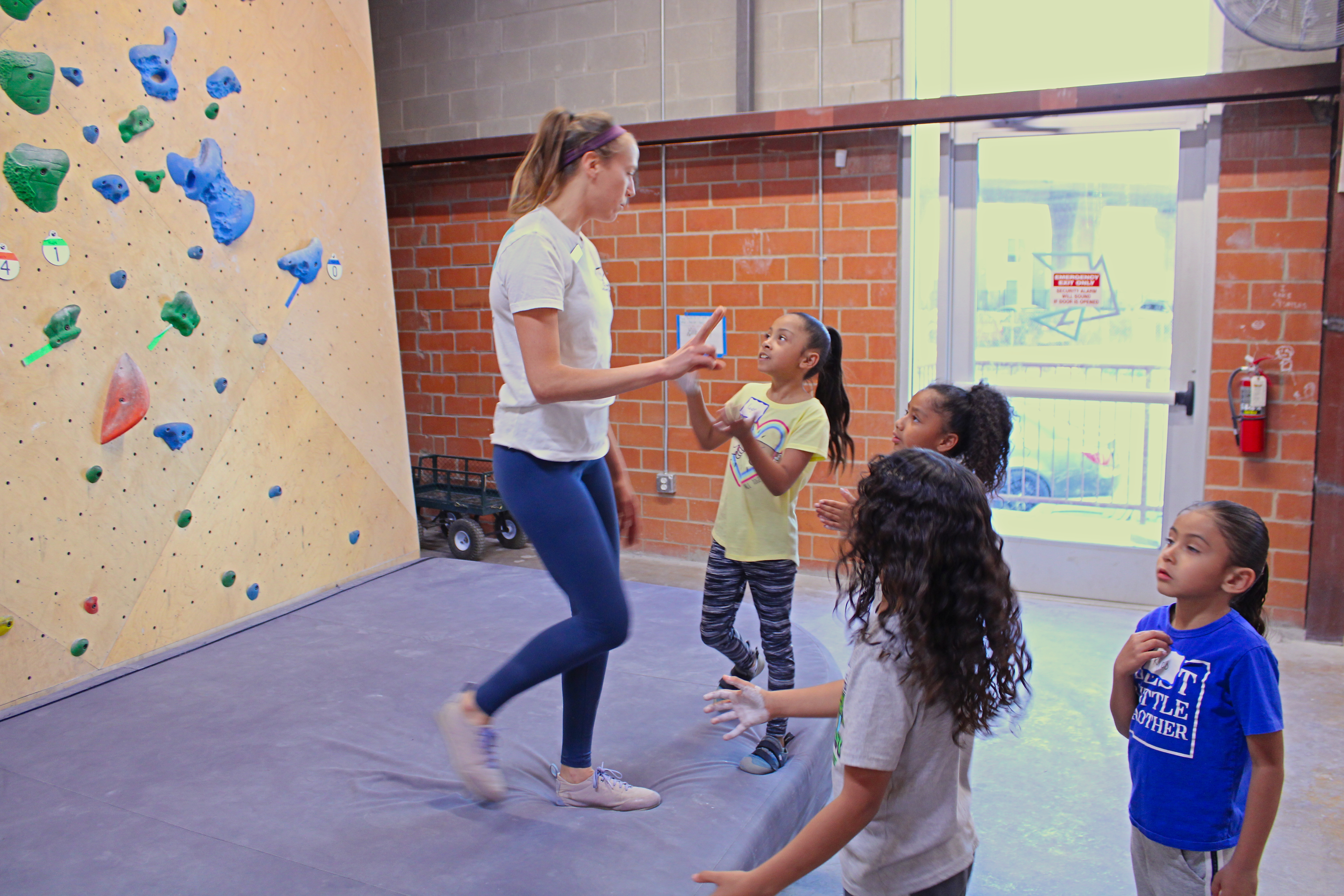 A group of young children stand at the base of a rock climbing wall