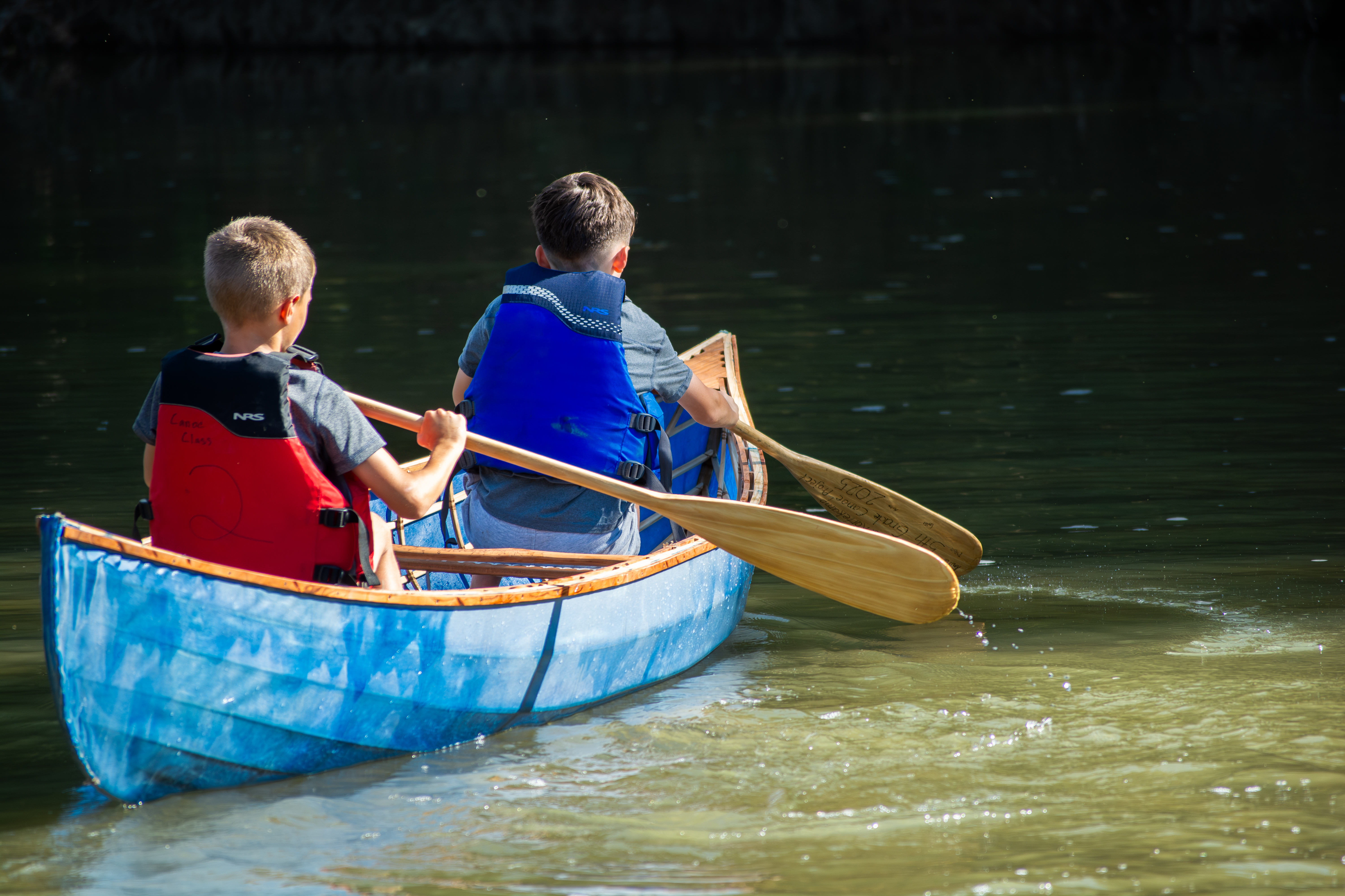 Two boys paddle a canoe together, backs to the camera