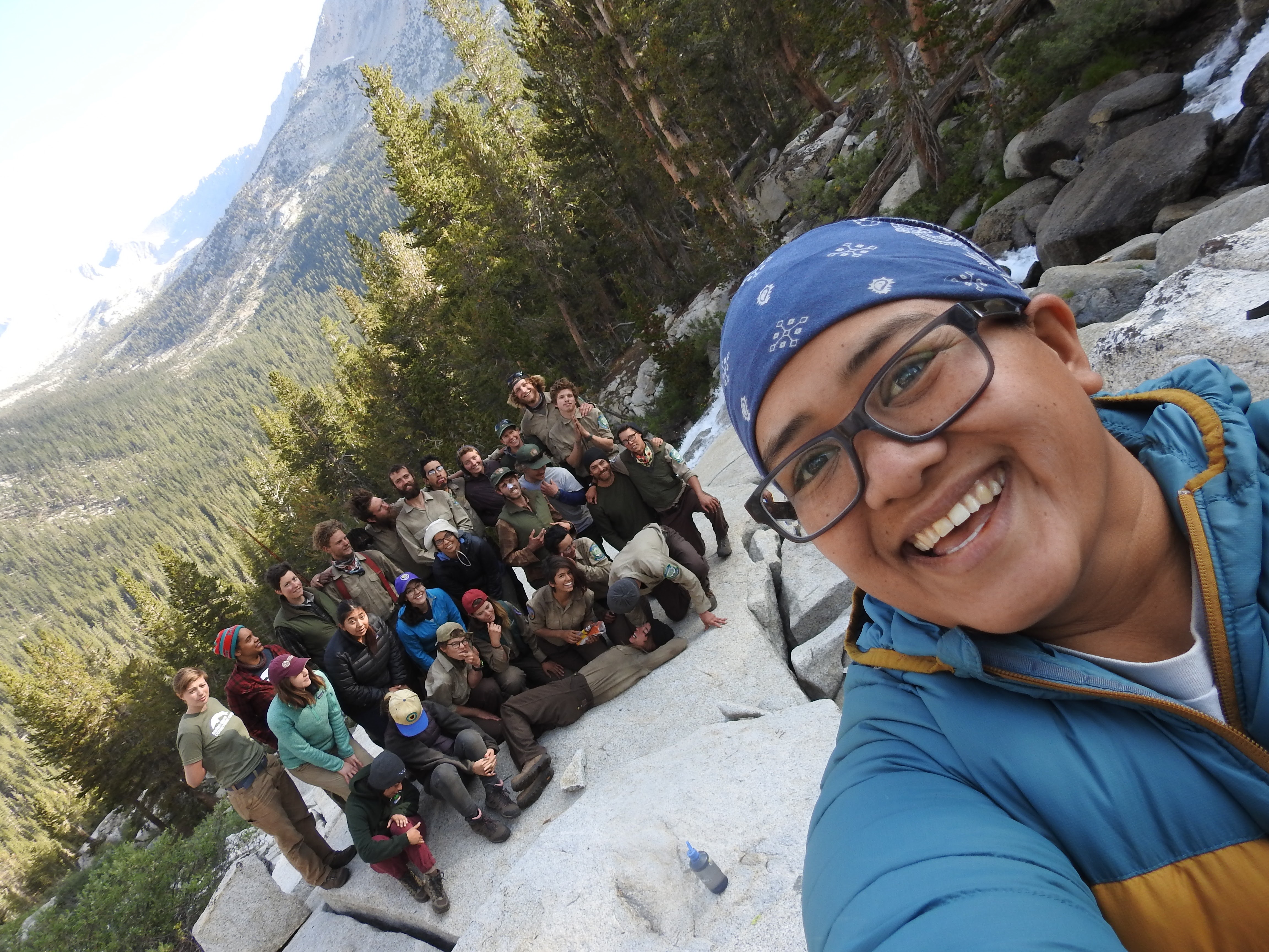 A person takes a selfie with a large group smiling in the background