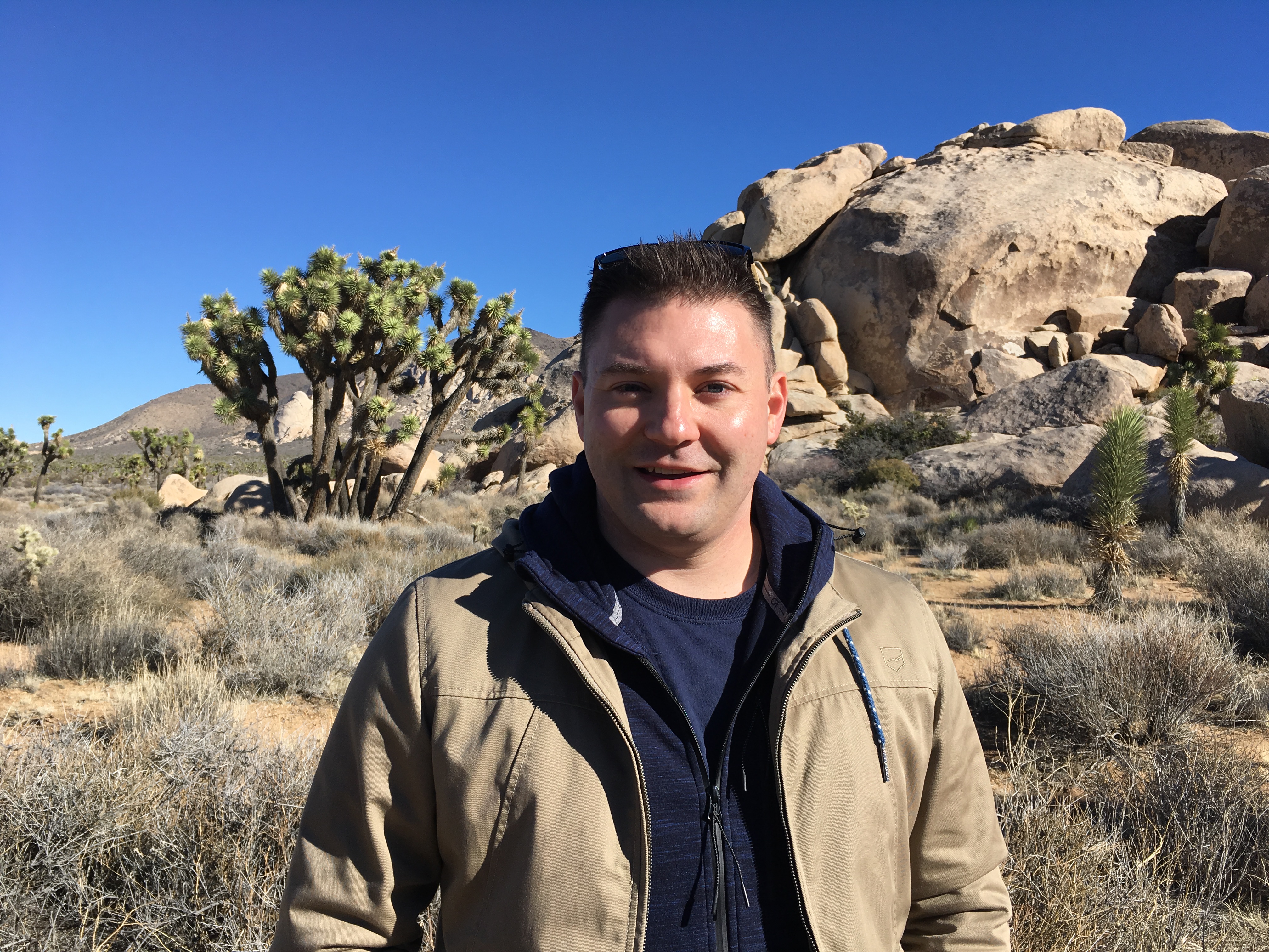 A man stands in front of a desert landscape and looks into the camera