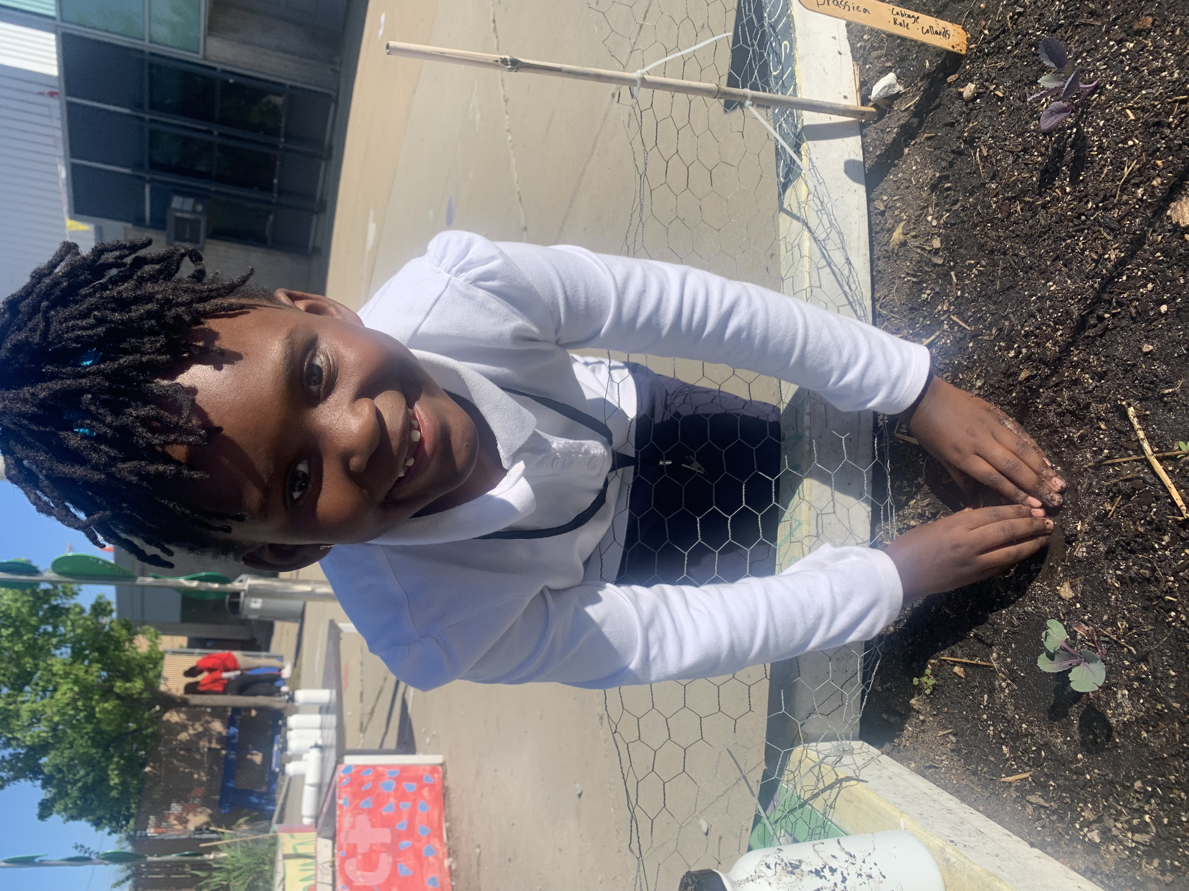 A student smiles while digging her hands in the dirt