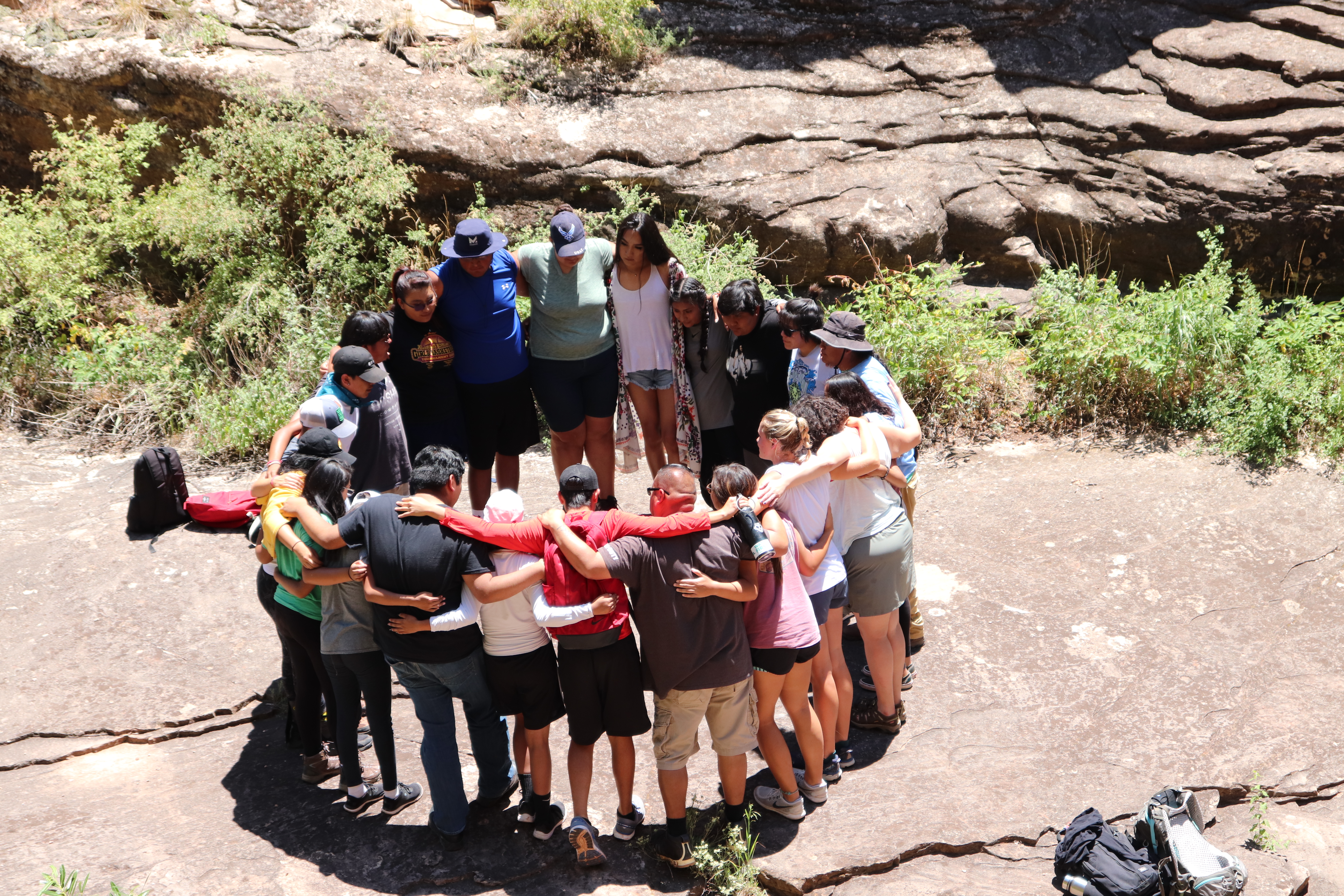 A group of people stand in a circle outside with their arms around each other