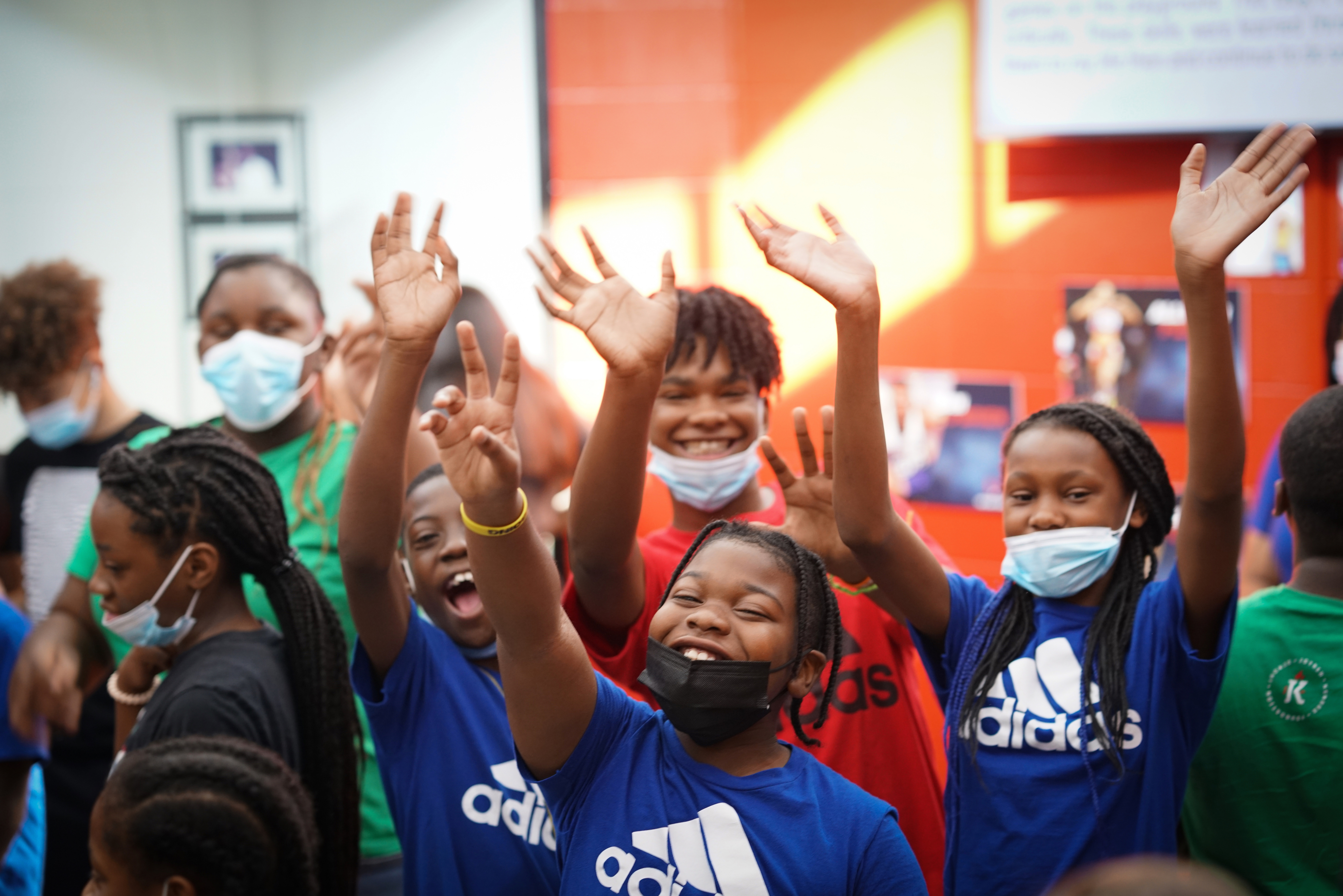 A group of youth smile and wave while wearing masks