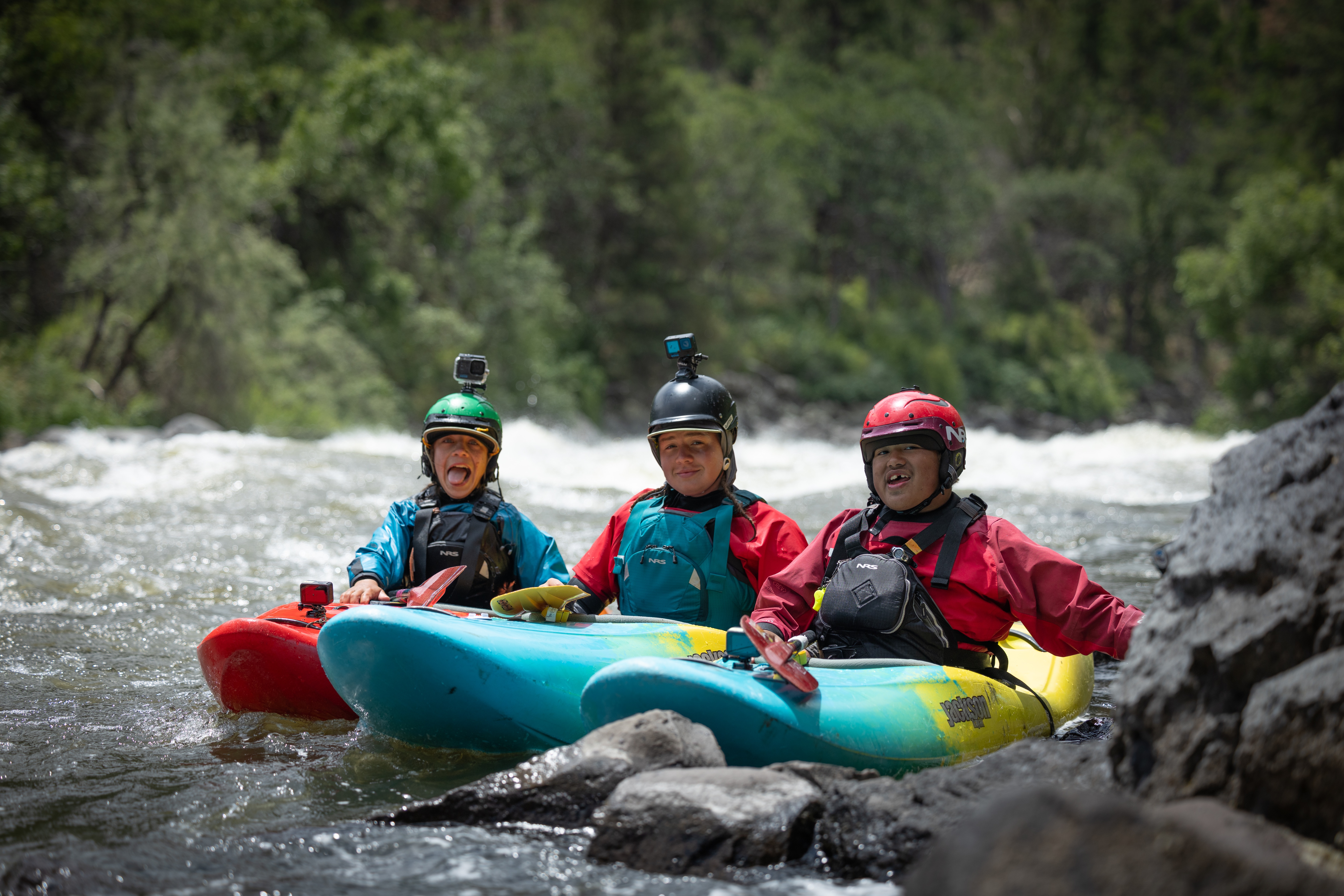 three youth sit in kayaks next to each other and smile