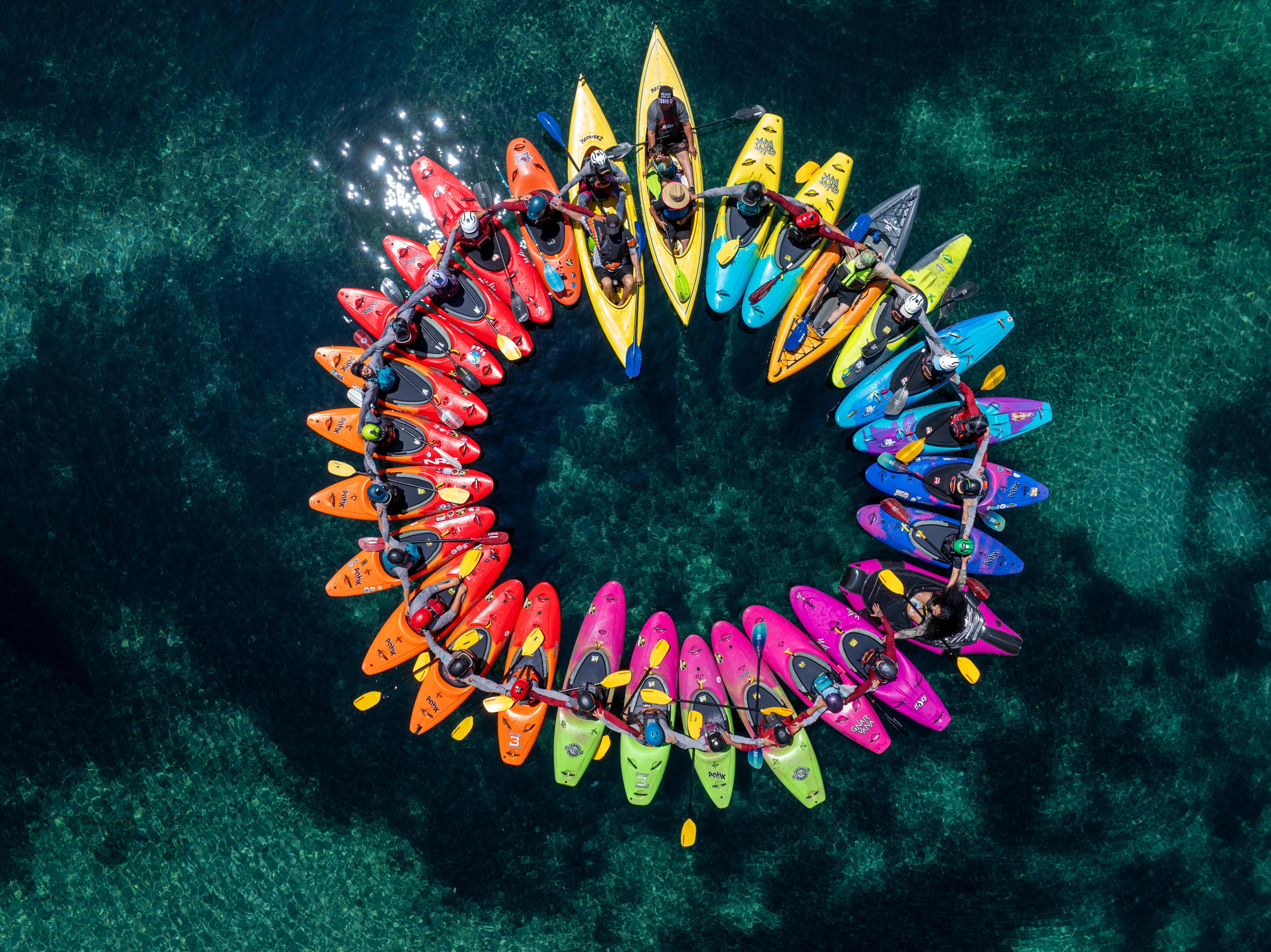 a group of kayakers have formed a circle with the kayaks making a rainbow on the water
