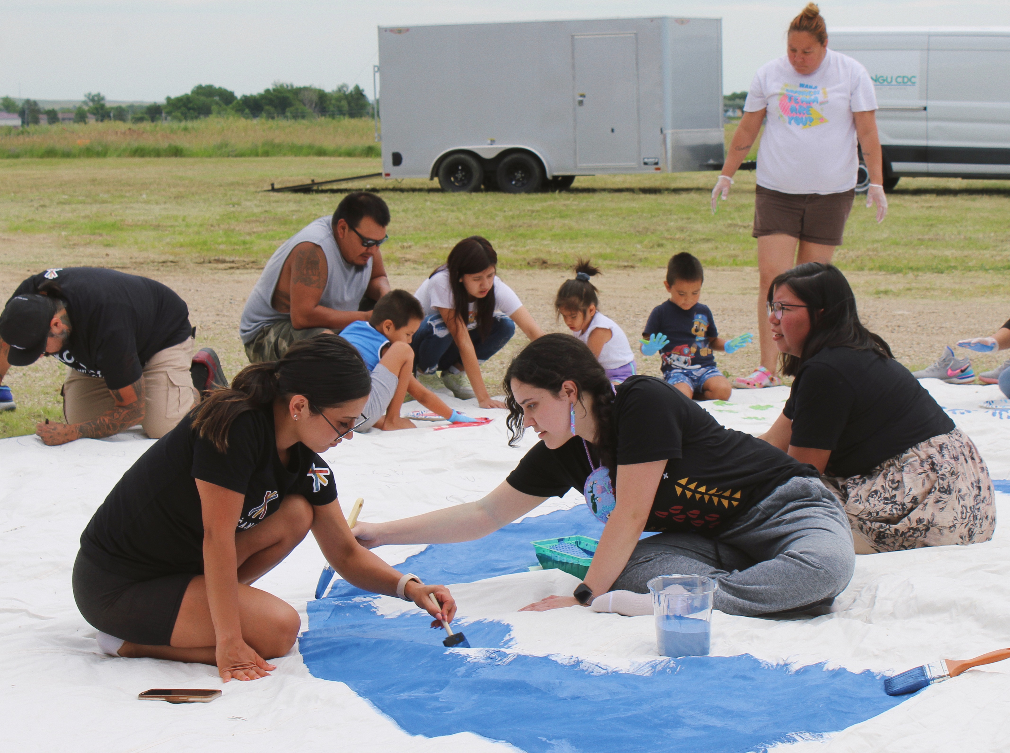 Young people sit on the ground painting together on a large shared canvas