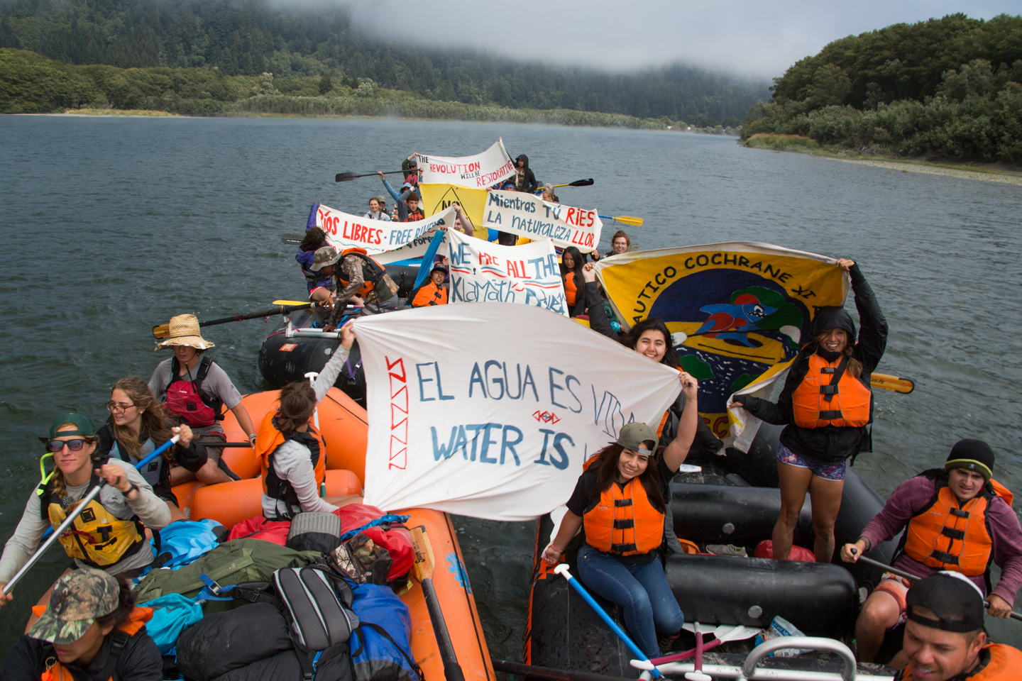 A group of people on rafts hold up signs protesting a dam