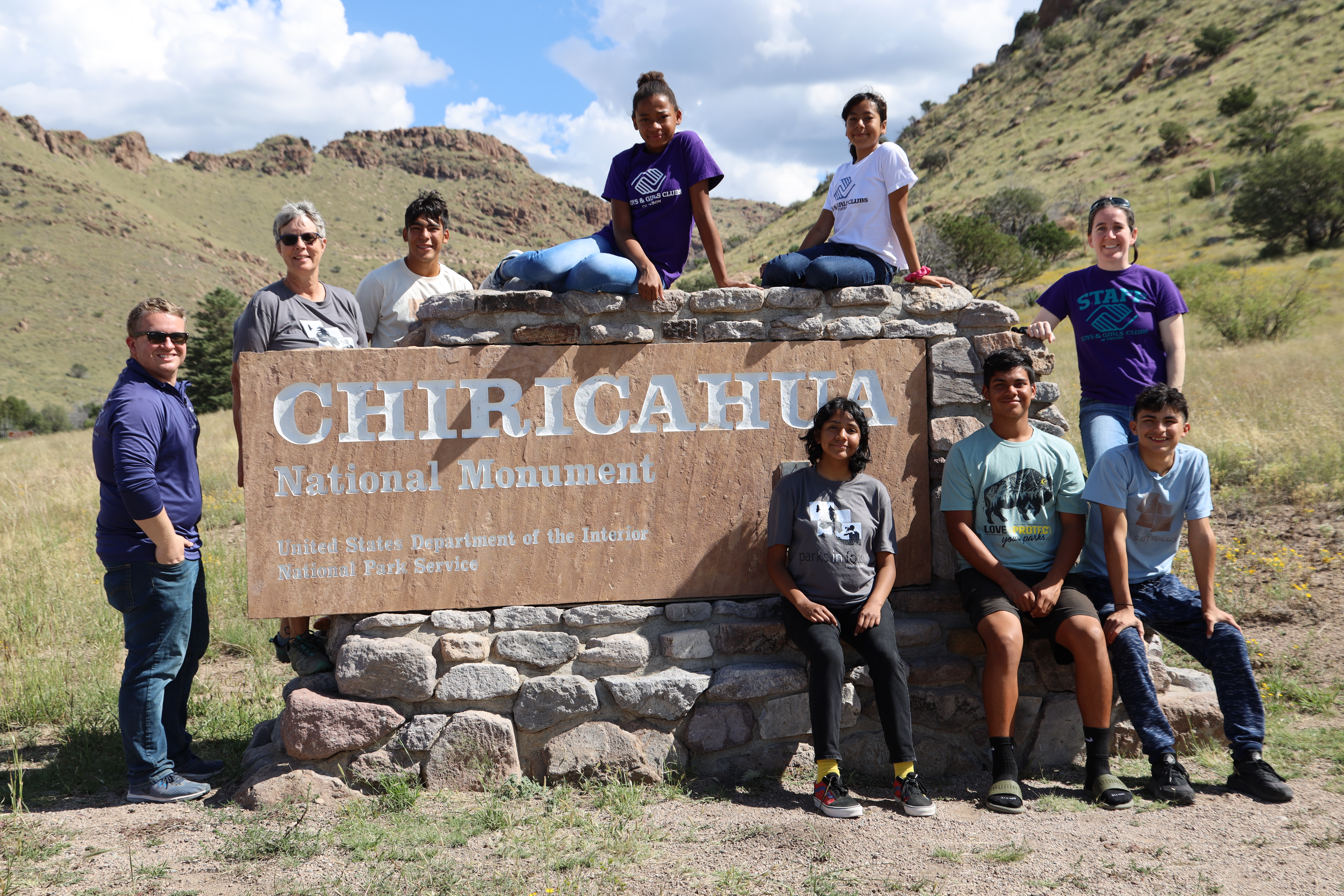 A group of adults and young people pose around a public lands sign